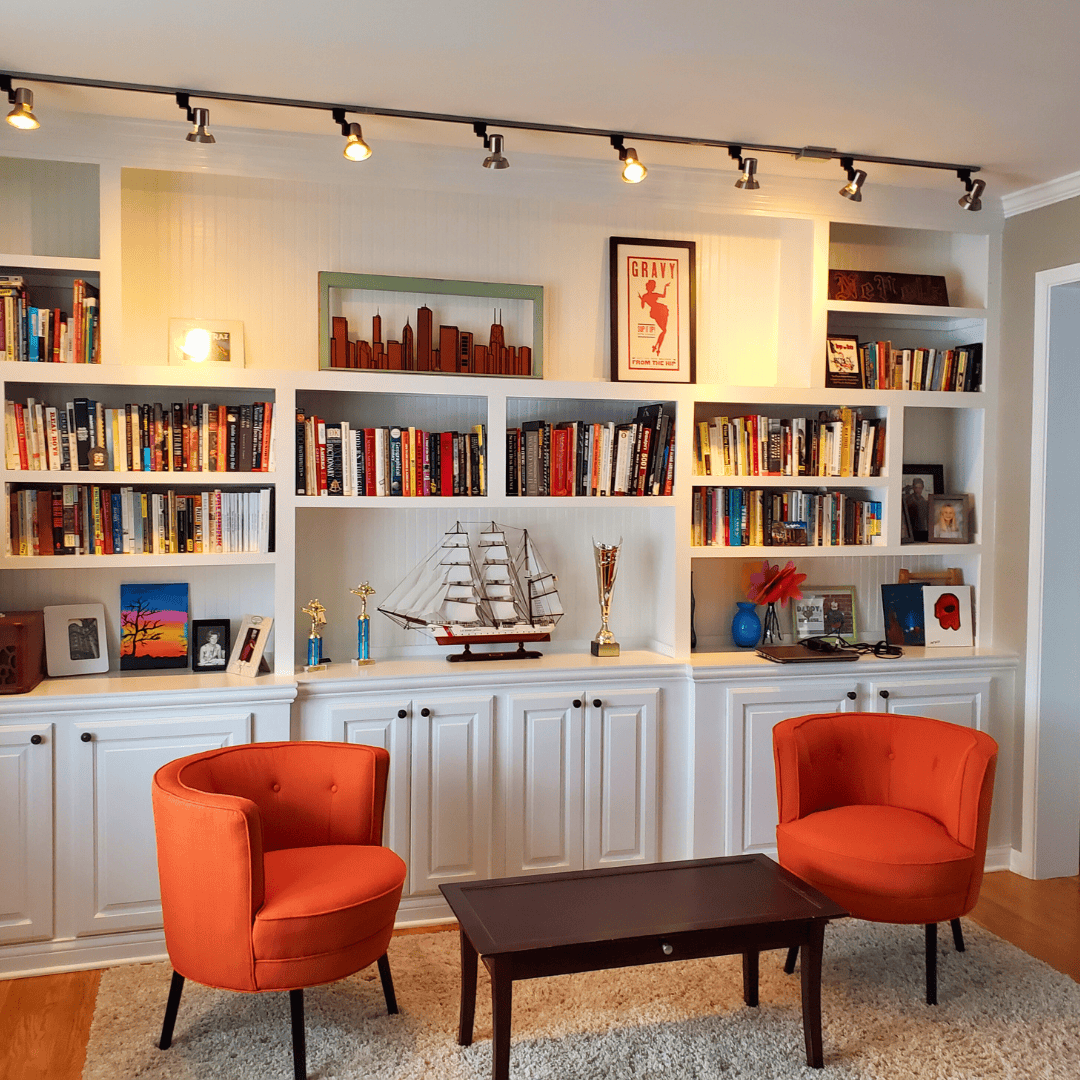 Comfortable orange armchairs in front of custom built-in bookshelves for home library design.