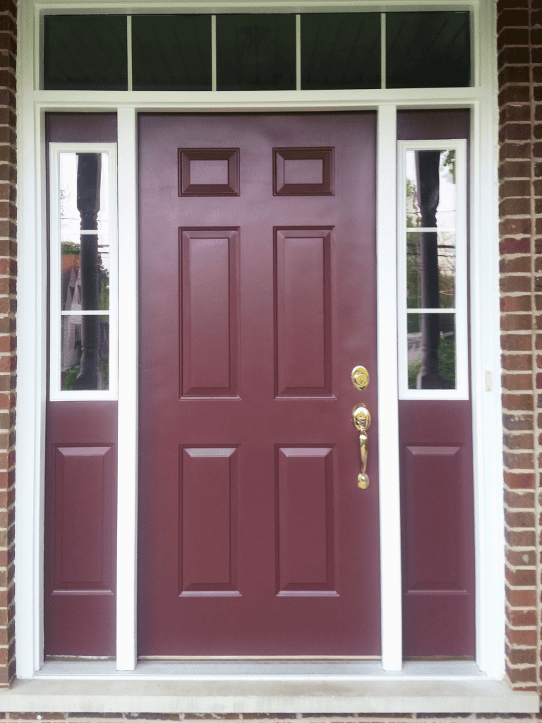 Elegant burgundy door with gold hardware, surrounded by white trim and brick exterior.